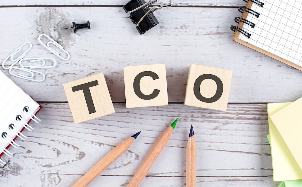 TCO - Total Cost of Ownership text on a wooden block with office tools on the wooden background